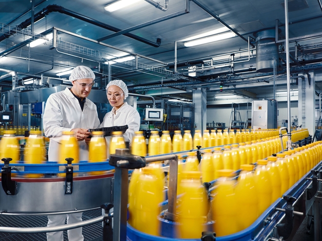 Dwóch inżynierów w fabryce napojów nadzoruje proces rozlewu soku pomarańczowego.